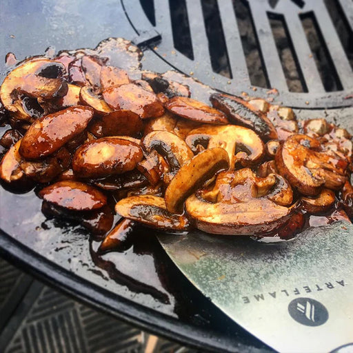 Arteflame stainless steel griddle spatula effortlessly flipping caramelized mushrooms on a flat top grill.