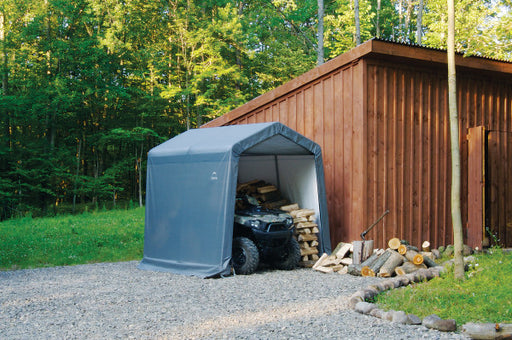An all-terrain vehicle (ATV) parked under a ShelterLogic tent next to a wooden storage shed