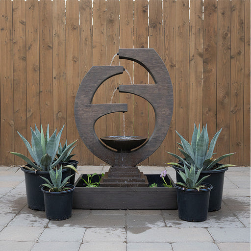 Backyard setting featuring Eclipse outdoor water fountain surrounded by potted agave plants against a wooden privacy fence.