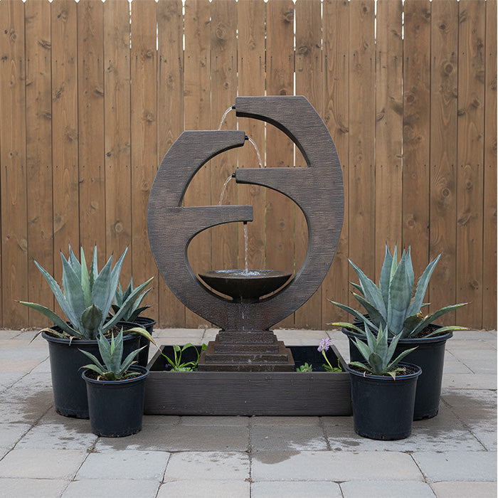 Backyard setting featuring Eclipse outdoor water fountain surrounded by potted agave plants against a wooden privacy fence.