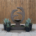 Backyard setting featuring Eclipse outdoor water fountain surrounded by potted agave plants against a wooden privacy fence.