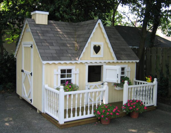  Beige cottage Victorian playhouse nestled in the backyard surrounded by colorful flowers.