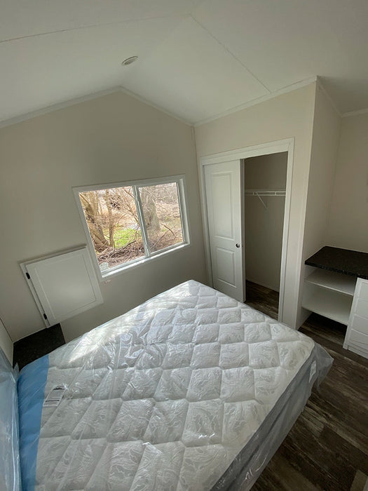 Newly set up bedroom in the Champion Home No Loft by Oasis Tiny Estates, with a bed and built-in shelving.