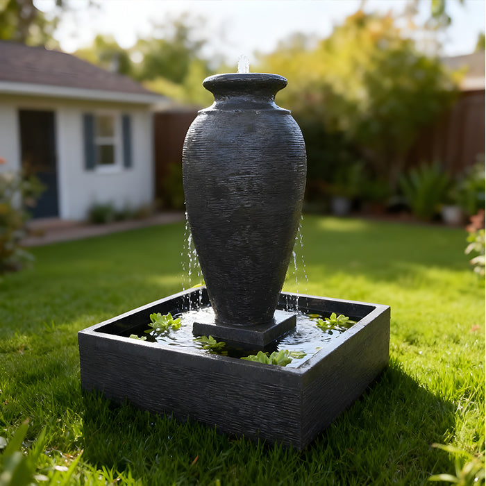 Black amphora fountain with square basin, gentle water flow and floating plants in contemporary backyard landscape.