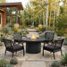 Real Flame Calvin 44" fire pit table burning on a modern concrete patio surrounded by agave and succulents, with a black wicker chair and contemporary home in the background