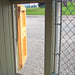 Interior view of the Cape Cod Cozy Kennel wooden door open to the outside, showing durable framing and chain-link fencing.