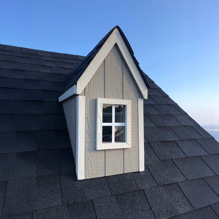 Close-up of a dormer window with white trim and gray shingles on the Little Cottage Co. Cape Cod Playhouse roof, highlighting charming architectural details.