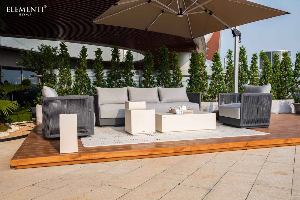 Full Elementi Capri Collection outdoor furniture set including sofa, chairs, and tables arranged elegantly on a modern patio under a large umbrella.