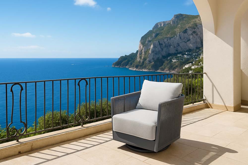 Elementi Capri Collection swivel chair set on a sunny balcony, overlooking a stunning ocean vista, featuring a gray frame and soft white cushions.