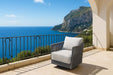 Elementi Capri Collection swivel chair set on a sunny balcony, overlooking a stunning ocean vista, featuring a gray frame and soft white cushions.