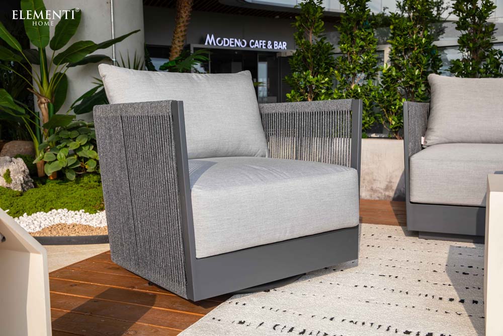 Elementi Capri Collection swivel chair displayed on a contemporary patio, featuring a sleek gray frame and soft gray cushions in lush garden setting.