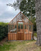 Alton Cedar Structure Cheltenham Greenhouse under tall trees with a shaded garden.