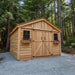 Front view of the Space Master 12x12 cedar storage shed with double doors closed, set on a gravel base outdoors.