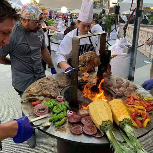 Chef preparing a variety of meats on an Arteflame Black Label Classic 40-inch grill with tall base during an outdoor culinary event.