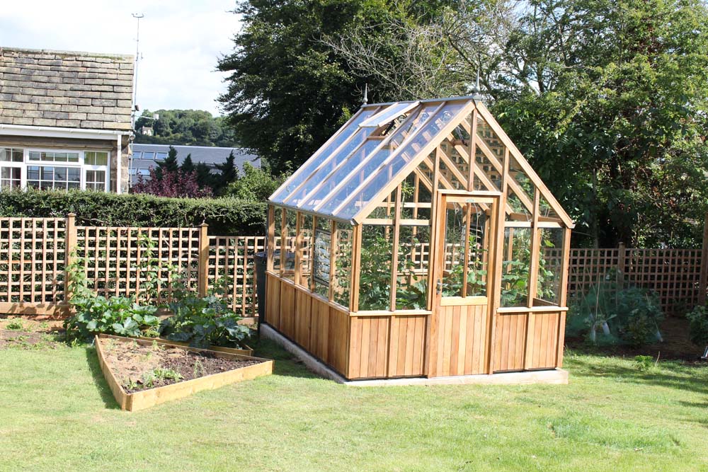 Alton Cheltenham Victorian Greenhouse in a suburban backyard surrounded by a lawn and vegetable patch.