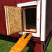Wooden ramp leading to a small chicken entry door on the red Little Cottage Co. Gambrel Barn Coop, shown with an open latch for easy access.