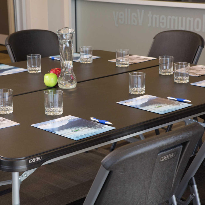 Lifetime 6-Foot Folding Table in black set up for meeting with chairs, glasses, and notepads