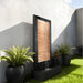 Contemporary backyard water fountain with copper slat design and dark frame, styled with potted plants on green lawn.