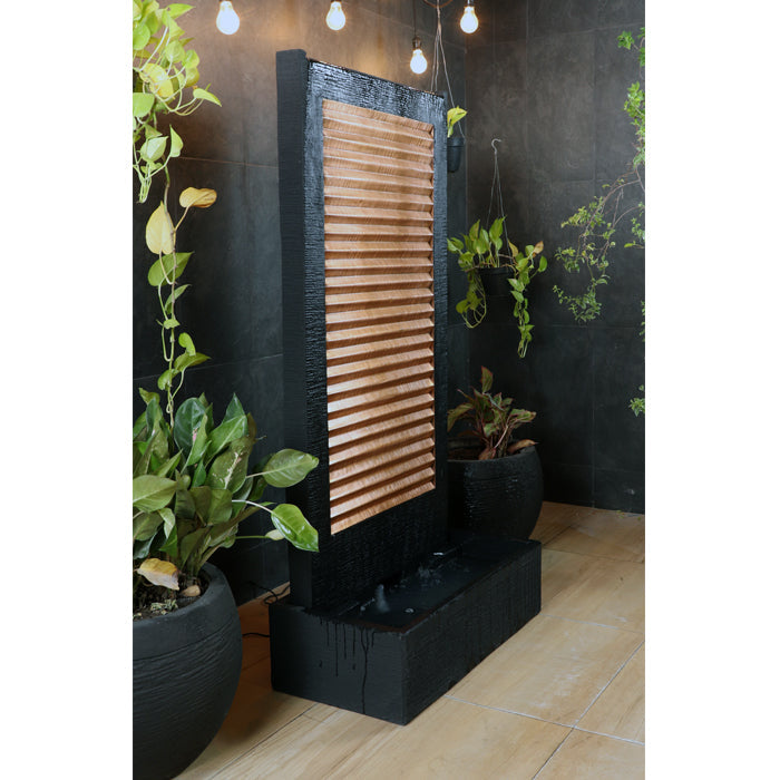 Contemporary waterfall wall fountain with copper accent panel and black frame, displayed on tiled patio with potted plants.