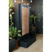 Contemporary waterfall wall fountain with copper accent panel and black frame, displayed on tiled patio with potted plants.