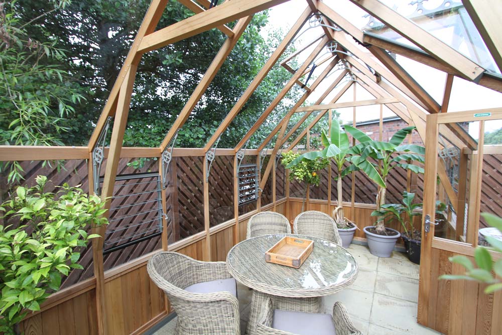 Cosy interior layout of the Alton Cambridge Cedar Greenhouse featuring potted plants and a glass dining table.