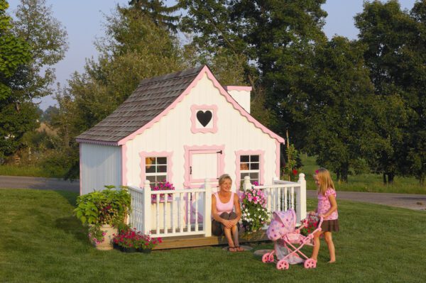 Young kids enjoying playtime in front of the Gingerbread Cottage Playhouse by Little Cottage Company, with vibrant flower pots.