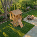 Aerial view of the Cozy Cabin Playhouse Kit 7x9 with rock climbing wall, sandbox, and ladder in a backyard setting