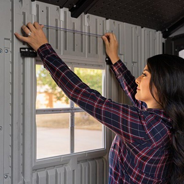 Interior view of the Lifetime storage shed's window frame with a person measuring for installation.