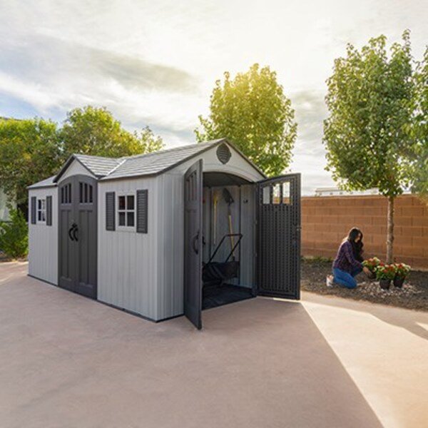 Lifetime dual entry storage shed with open side door, woman gardening in the background.