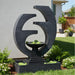 Close-up of black Eclipse contemporary outdoor water fountain with circular frame and bowl basin, installed beside home exterior.