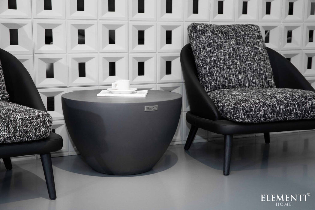 Elementi Chronos Series small coffee table in slate black, styled between two accent chairs in a modern room setting.