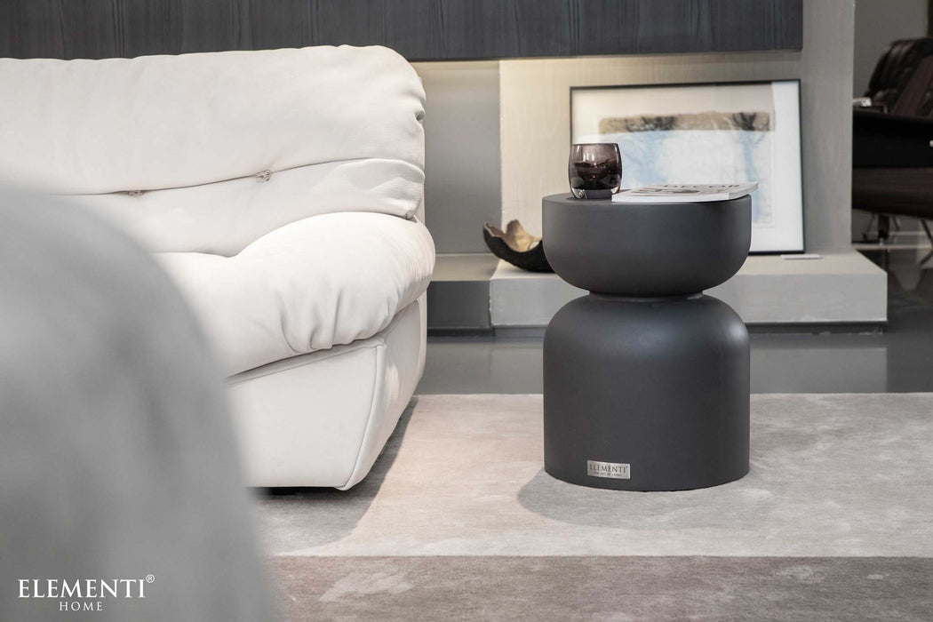 Elementi Chronos Series small side table in slate black, styled next to a white couch in a modern living room setting.