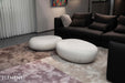 Elementi Hawaii Pebble Table series in cream white, displayed in a modern living room with a black couch and textured rug.