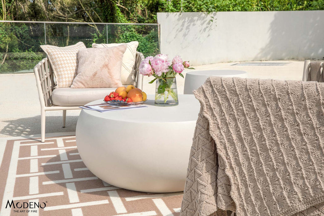 Elementi Ikaria Coffee Table Cream White in an outdoor scene featuring cozy seating arrangements and lush greenery in the background.