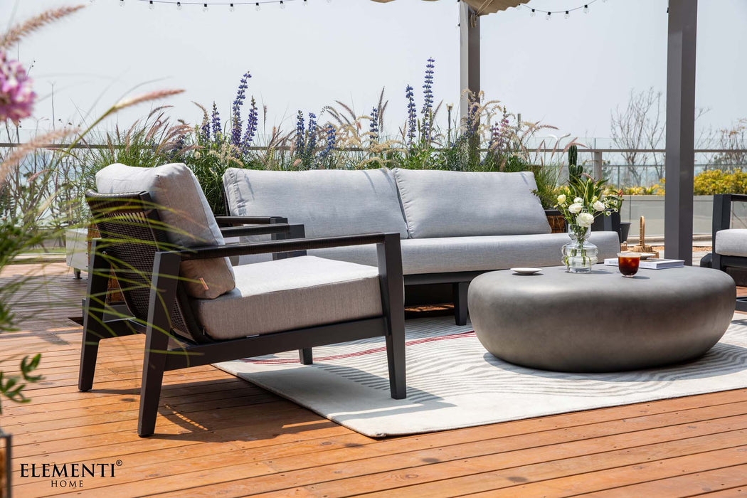 Elementi Laguna Collection furniture on a sunlit wooden deck, featuring a sofa, chair, and a unique round coffee table in an outdoor space.