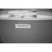 The Elementi nameplate badge reading 'The Art of Living' is mounted on the curved gray concrete exterior of the fire bowl, shown in a soft-focus black-and-white close-up with the burner ring blurred in the background above.