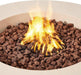 Extreme macro close-up of bright orange and yellow flames rising through reddish-brown lava rocks inside the cream white concrete basin of the Elementi Lunar Bowl Fire Table, showcasing the smokeless burner flame pattern and volcanic rock media in detail.
