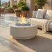 Elementi Nimes fire pit table burning with glass wind guard installed, set on a stone patio beside a cushioned outdoor sofa