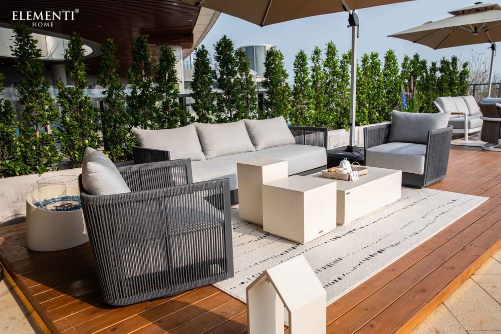 Luxury outdoor patio featuring Elementi Capri Collection sofa and chairs paired elegantly with modern tables and lush greenery in a stylish setting.