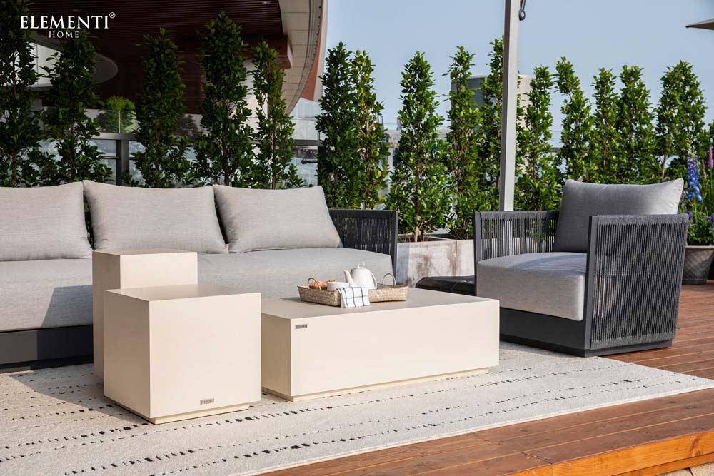 Stylish outdoor arrangement featuring Capri Collection sofa, chair, and coffee tables by Elementi set against a backdrop of greenery on a wooden deck.