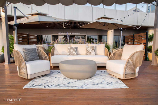 Complete view of Elementi Outdoor Furnitures Malibu Collection featuring a full patio setup with neutral chairs, sofa, and center coffee table on a deck.

