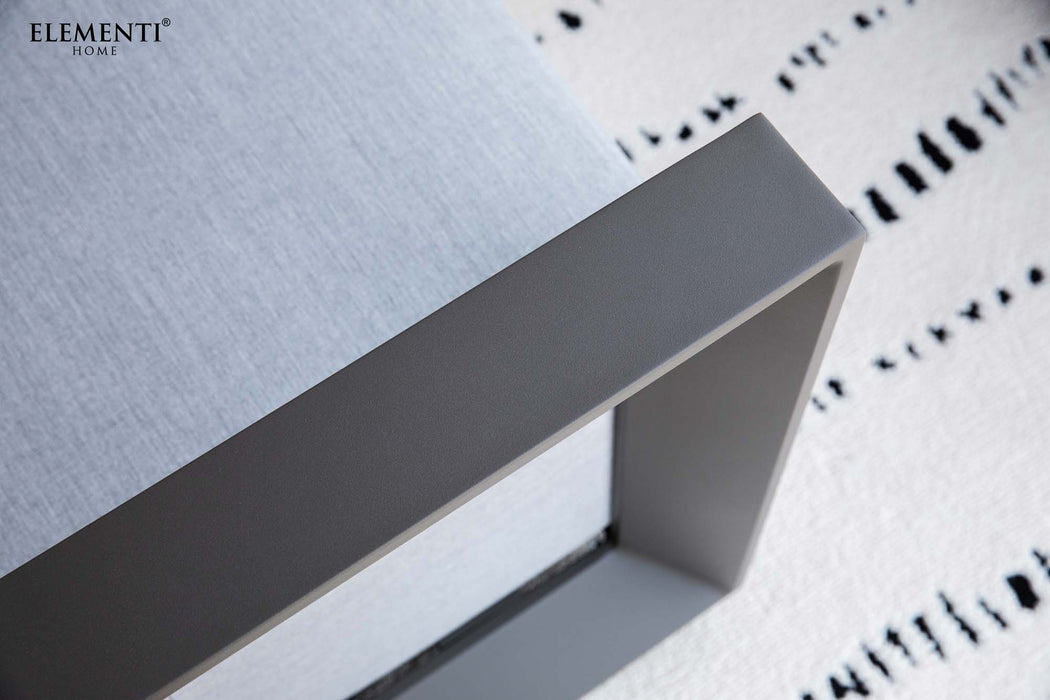 Detailed shot of the Elementi Outdoor Furnitures Newport Collection's sturdy grey frame and light cushion, on a patterned rug.