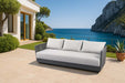 Luxurious Capri Collection outdoor sofa by Elementi placed in an elegant seaside patio, featuring plush white cushions contrasting against a gray frame.