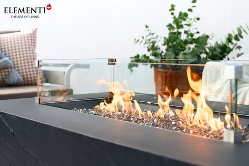 Angled view of Elementi Plus Rectangular Wind Screen OFG410/415-WS on a dark outdoor fire pit table, with flames contained by glass.