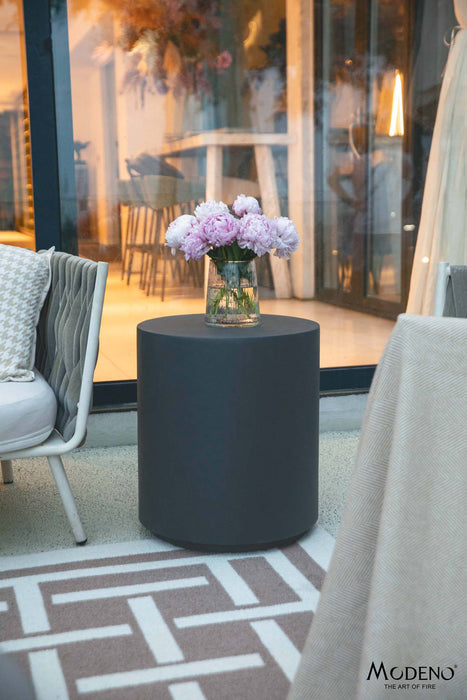 Elementi Rome Slate Black Side Table displayed in an outdoor setting with flowers, enhancing the overall aesthetic of the patio area.