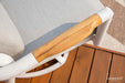 An overhead view of a light brown wooden armrest on a white frame, with a light gray cushion in the background, from the Santorini Collection.

