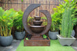 Brown Exaco Eclipse Fountain with a three-tiered water feature, bringing a modern and elegant touch to any outdoor garden space with surrounding greenery and bamboo fencing.