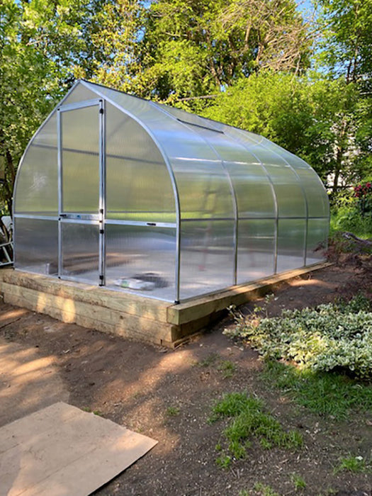 Fully assembled Exaco Hoklartherm Riga Greenhouse 4 with twin-wall polycarbonate panels, built on a raised wooden base in a backyard garden.