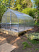 Fully assembled Exaco Hoklartherm Riga Greenhouse 4 with twin-wall polycarbonate panels, built on a raised wooden base in a backyard garden.