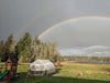 Exaco Hoklartherm Riga XL 6 Greenhouse in an open field beneath a double rainbow, blending natural beauty with durable year-round gardening design.